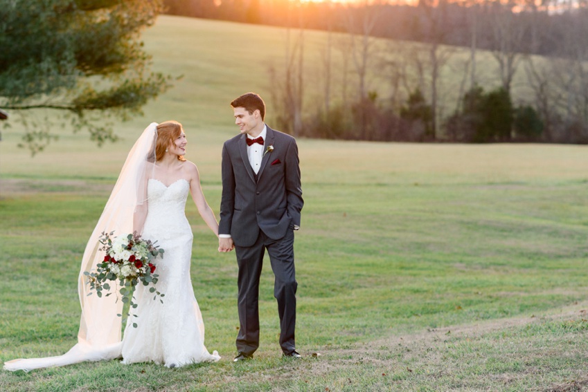 bride and groom walking in field at sunset