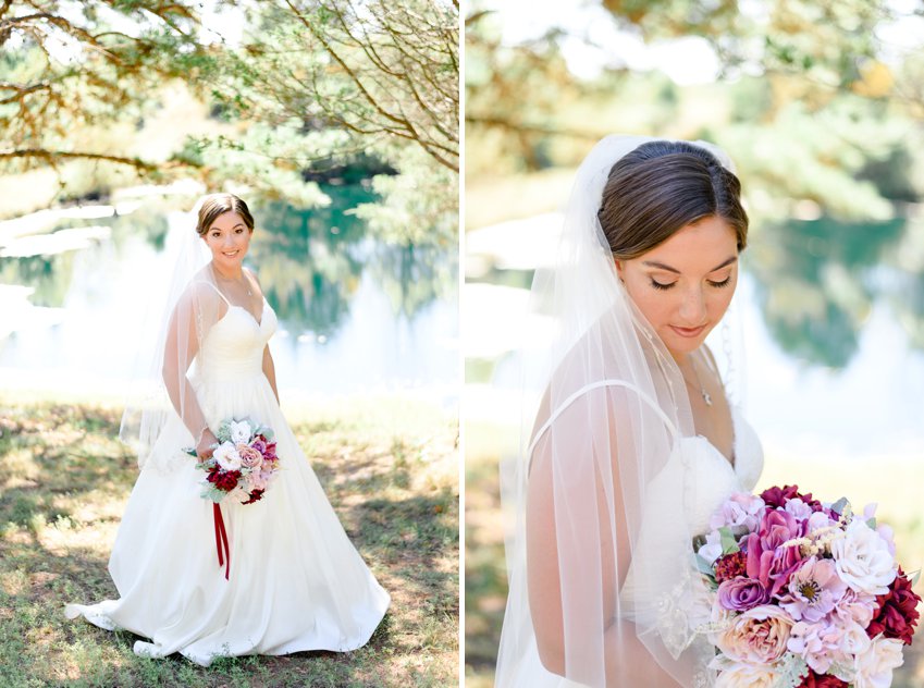 bride holding deep red flower bouquet in front of blue pond