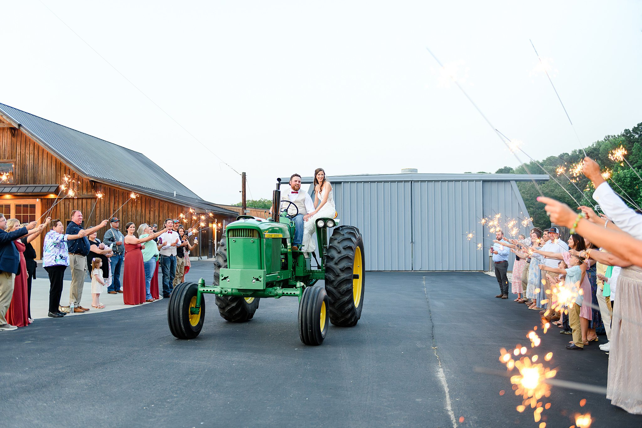 Sparkler exit with rustic charm as bride and groom ride past friends and family on a tractor